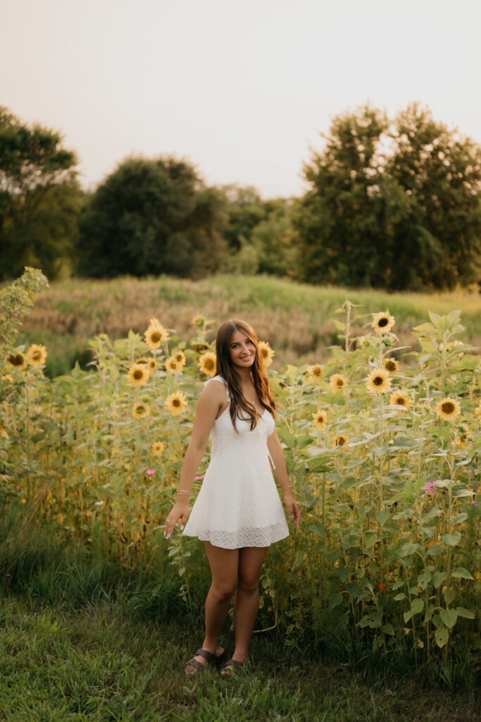 Senior girl in white dress standing in sunflower field at Pixel Dust Acres