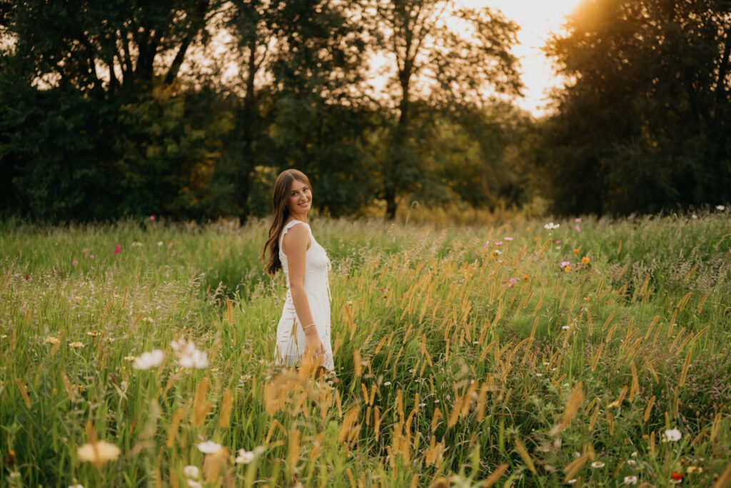Senior girl in white dress walking away through tall grass field at Pixel Dust Acres