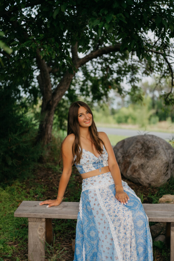 Senior girl in blue floral two-piece sitting on wooden bench at Pixel Dust Acres