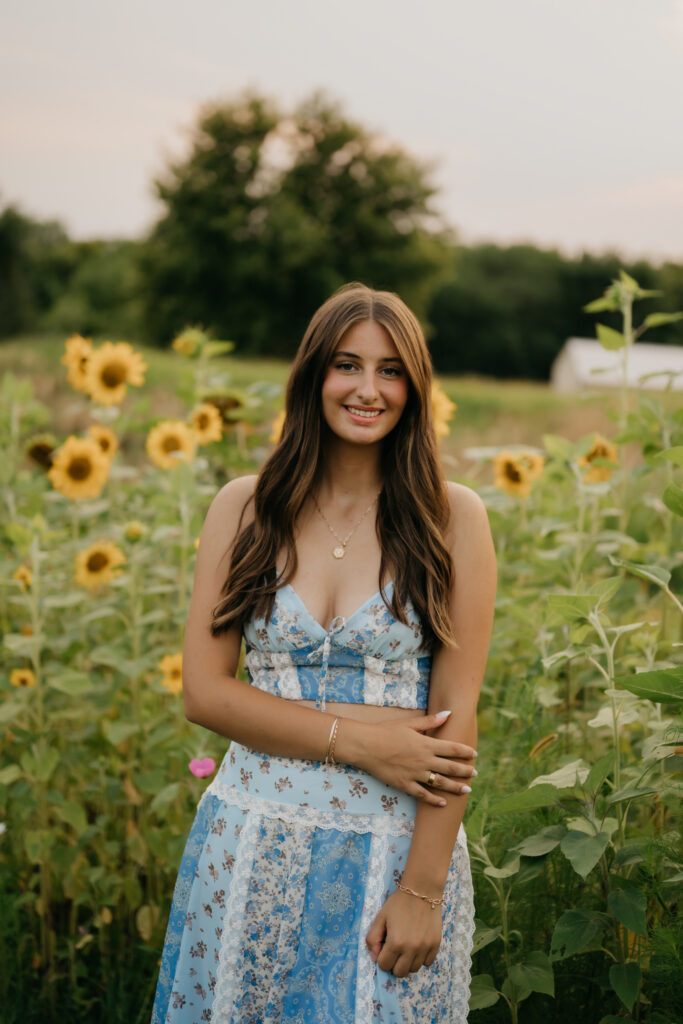 Senior girl in blue floral two-piece standing in sunflower field at Pixel Dust Acres