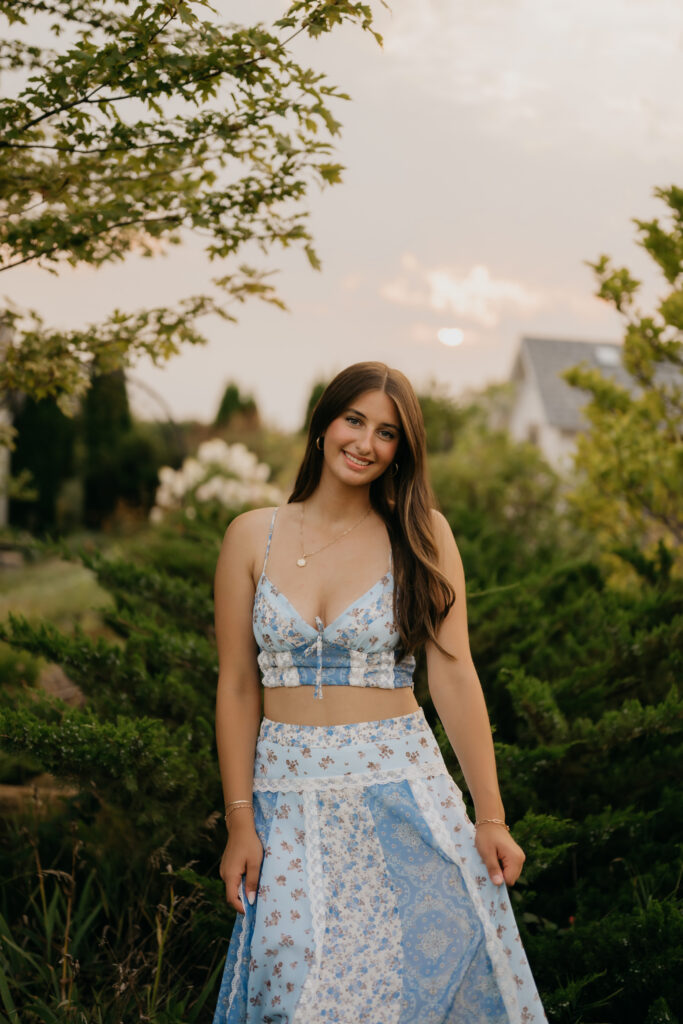 Senior girl in blue floral two-piece standing near garden hedges at Pixel Dust Acres