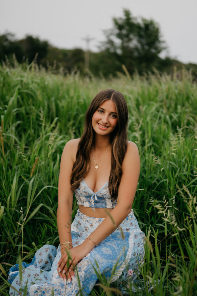 Senior girl in blue floral two-piece smiling in tall grass field at Pixel Dust Acres