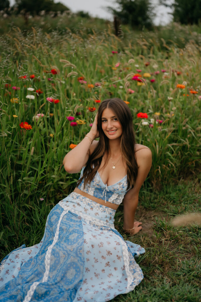 Senior girl in blue floral outfit sitting among poppies at Pixel Dust Acres