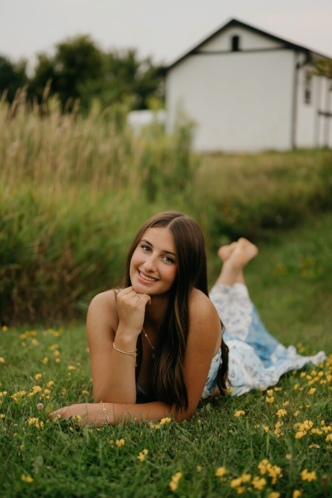 Senior girl in blue floral dress lying in grass among wildflowers at Pixel Dust Acres