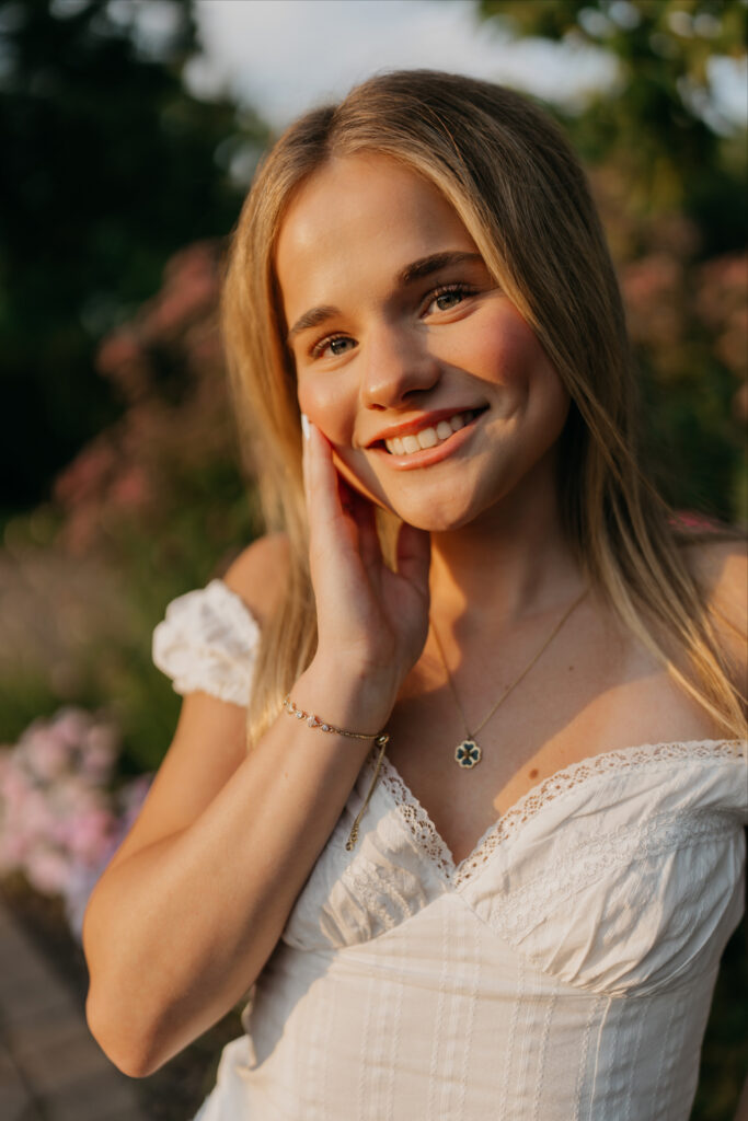 Senior smiling with hand near her face, wearing an off-shoulder white top