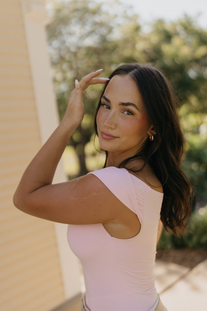 Senior girl in pink top touching her hair on a sunlit garden patio