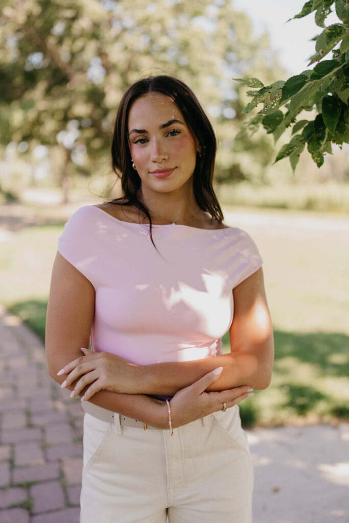 Senior girl in pink off-shoulder top with arms crossed under a tree