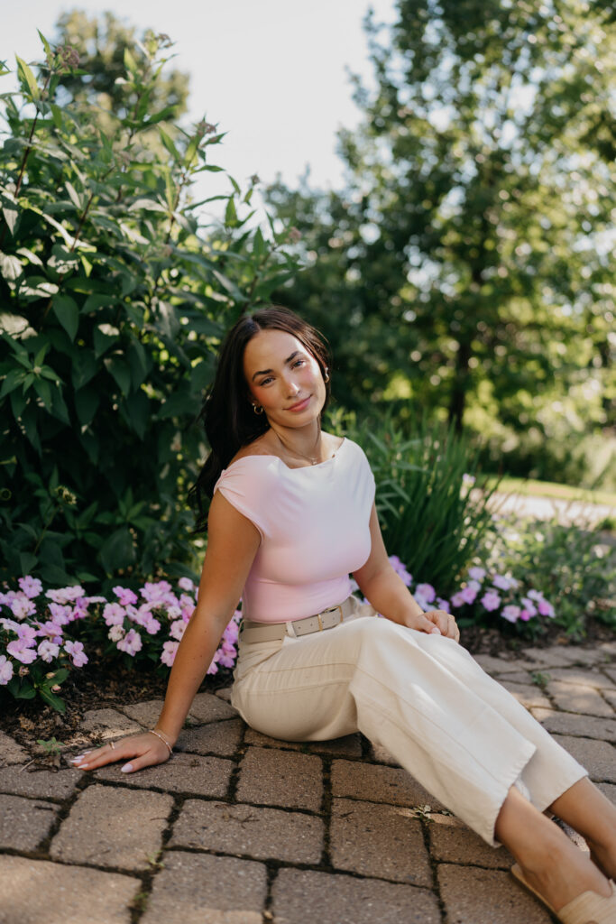 Senior girl in cream top sitting on brick pavers among purple flowers