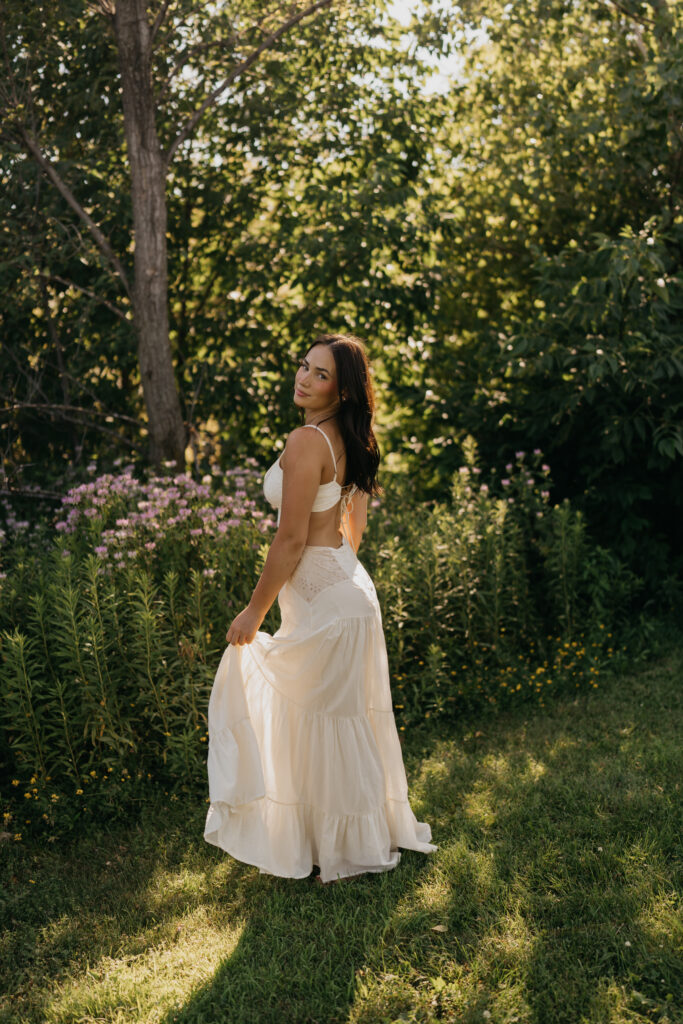 Senior girl in a cream backless dress standing in a wildflower meadow