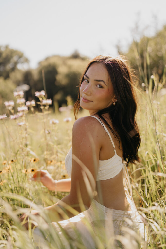 Senior girl in a cream backless dress in tall grass with hand near her hair