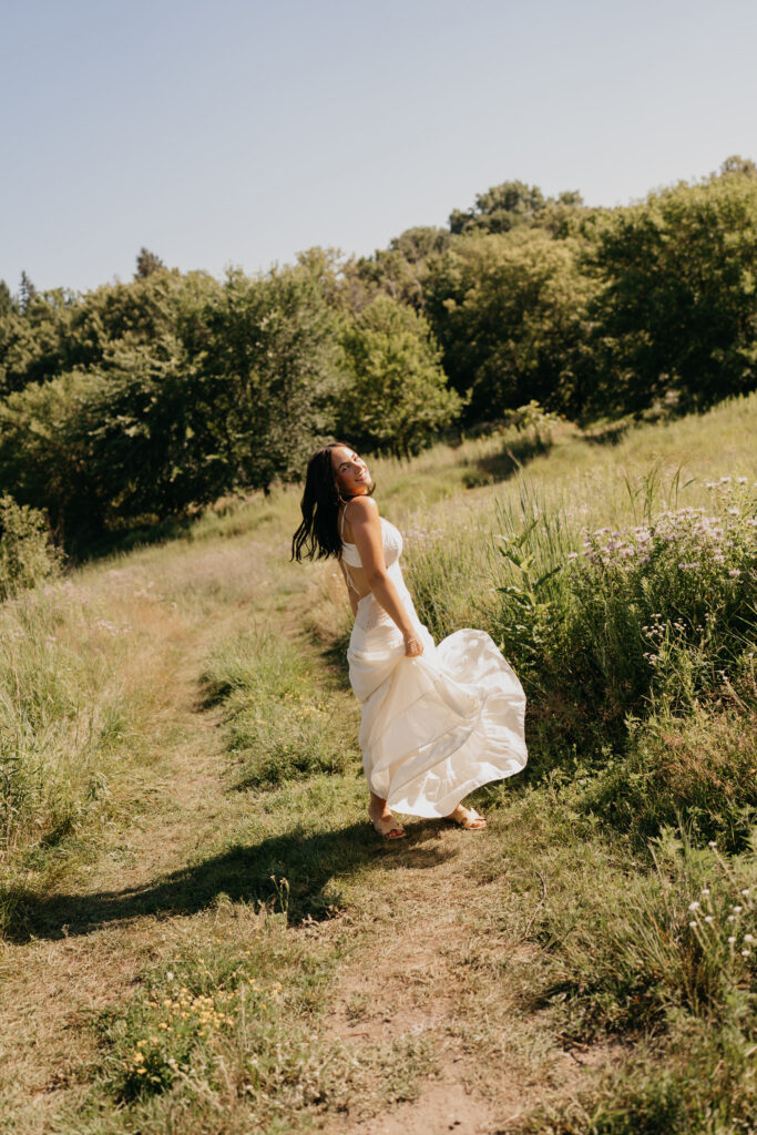 Senior girl in a flowing white dress caught mid-stride on a grassy path