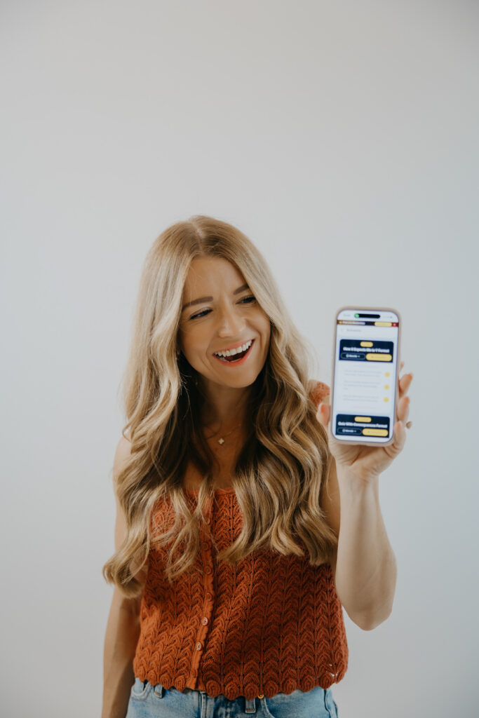 Meg Jackson laughing while holding up a smartphone displaying an app interface
