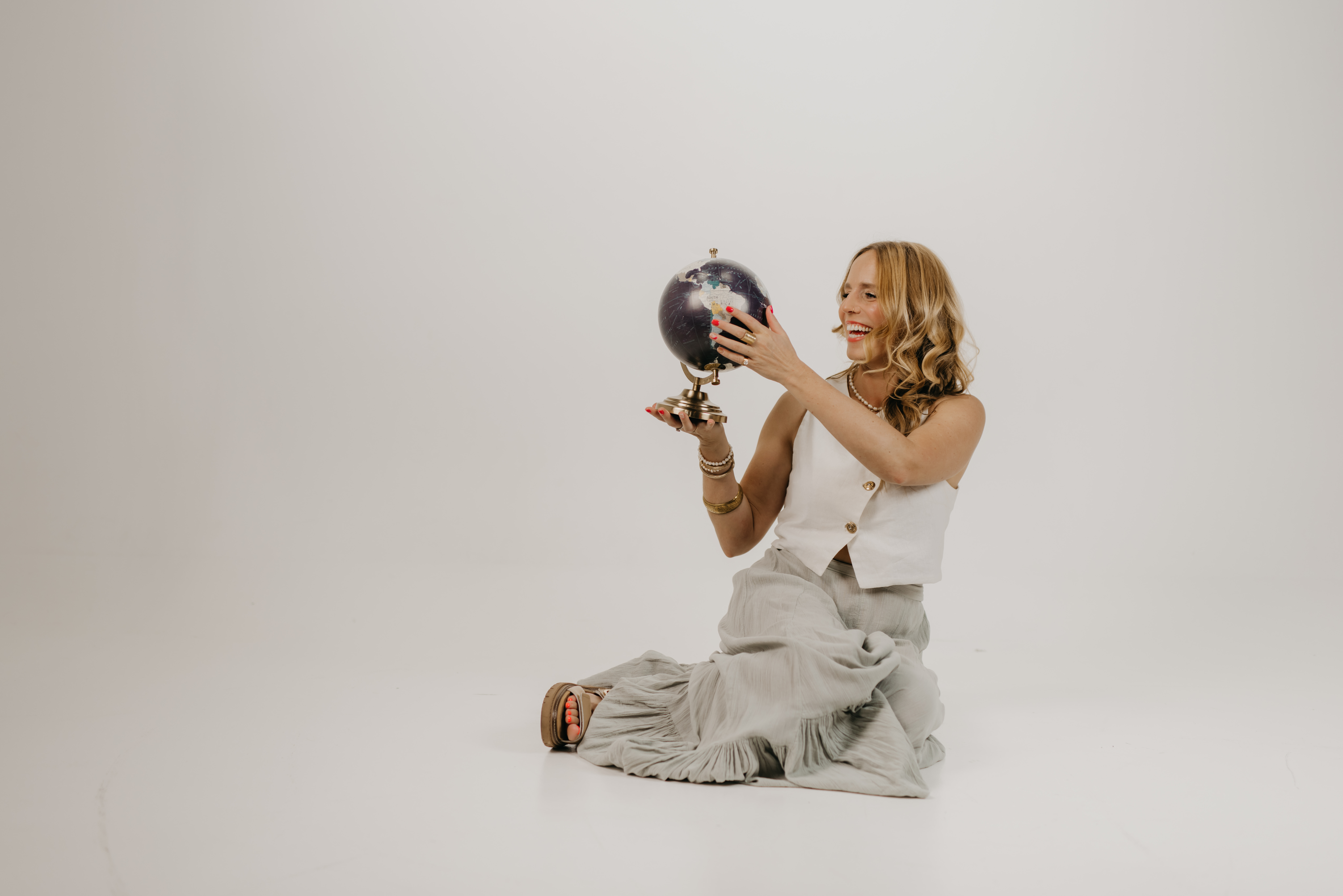 Brand photography detail shot of a woman laughing while holding a vintage globe, an example of personal branding photo ideas that show personality