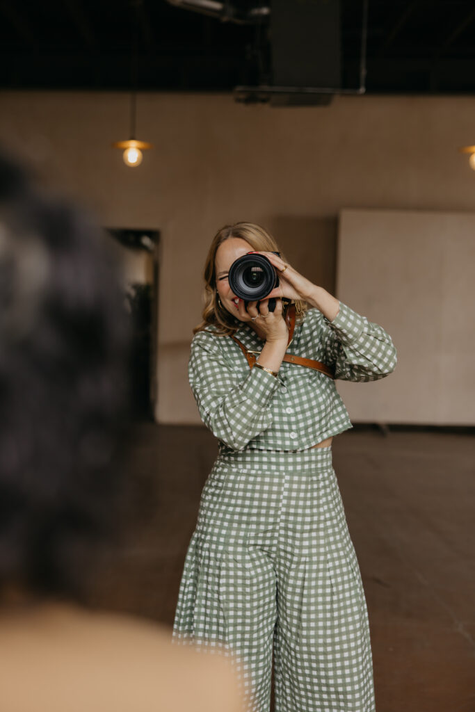 Woman in a green gingham jumpsuit photographing a subject up close