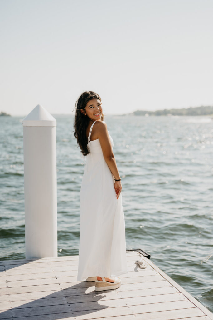 Natalia standing in a white dress on a dock with the lake behind her