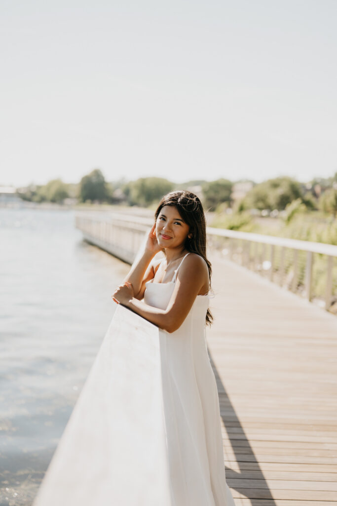 Natalia leaning against a dock railing in a white dress overlooking the water