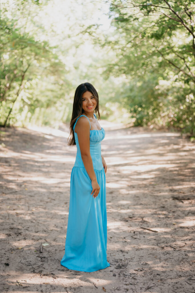 Natalia walking down a sunlit path in a blue satin dress