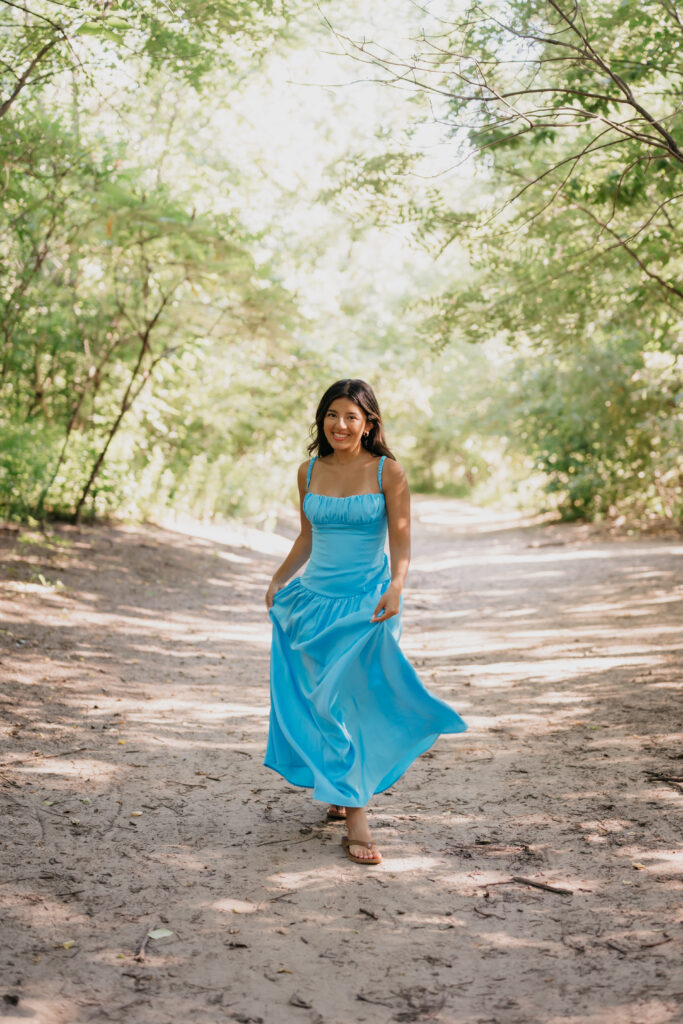Natalia twirling on a wooded path in a blue satin dress