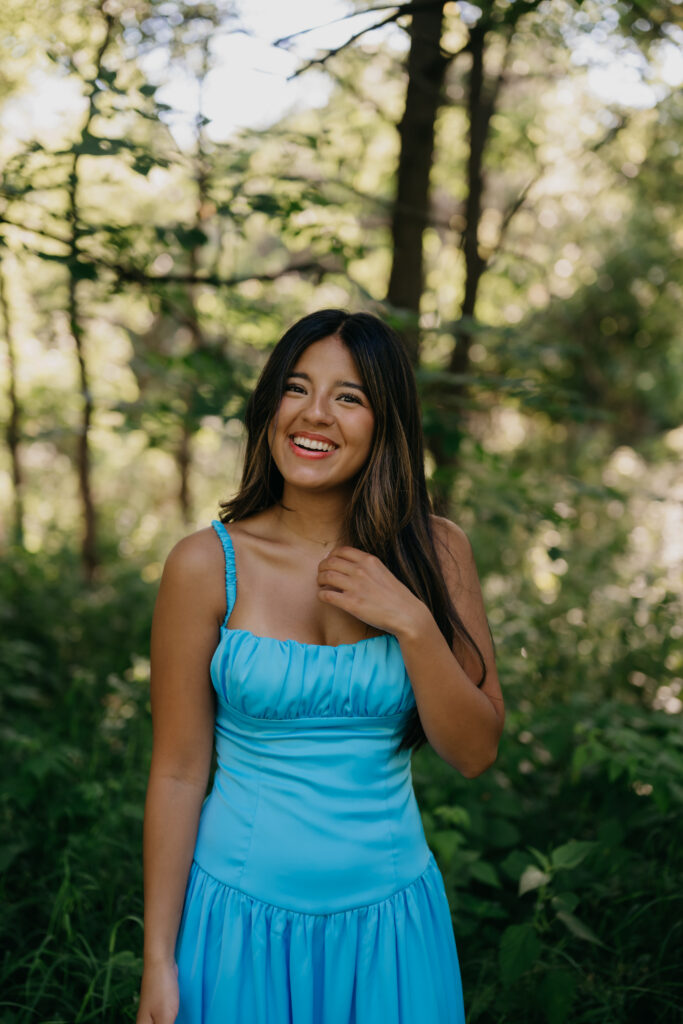 Natalia smiling in a blue satin dress surrounded by trees