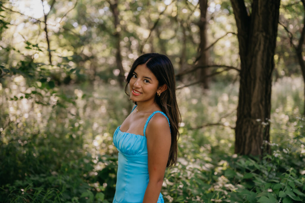 Natalia smiling in a blue satin dress surrounded by trees during her senior session