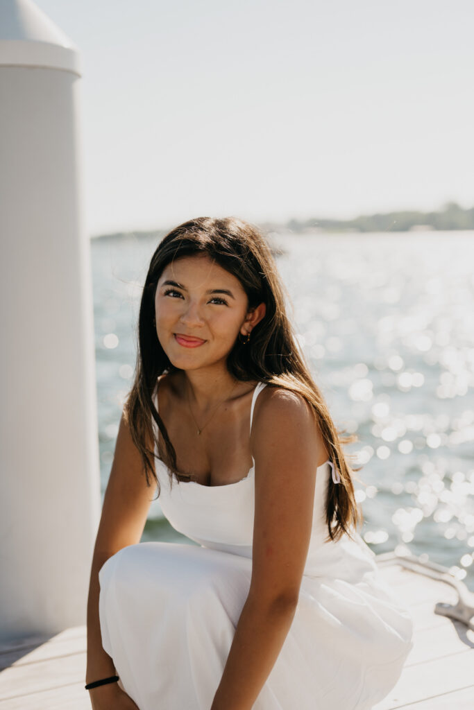 Natalia crouching in a white dress on a dock overlooking the water in Minneapolis