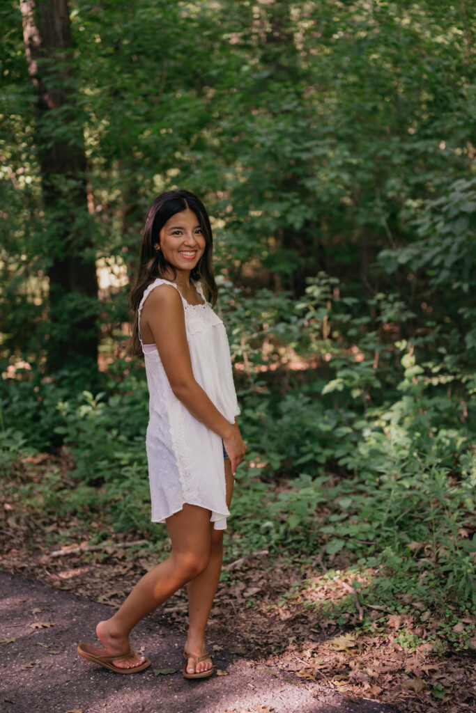 Natalia walking down a wooded path in a white dress during her senior session