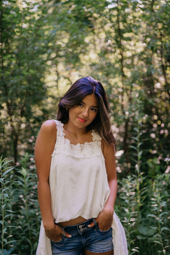 Natalia smiling in a white eyelet top and denim shorts during her senior photo session