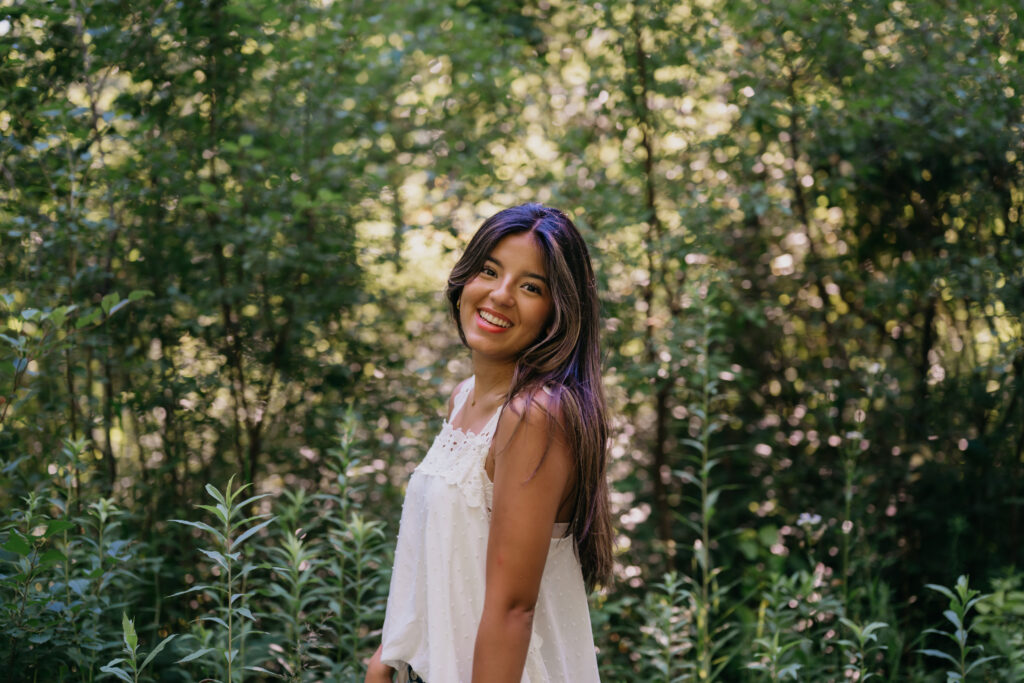 Natalia smiling in a white eyelet top in a wooded Minneapolis location