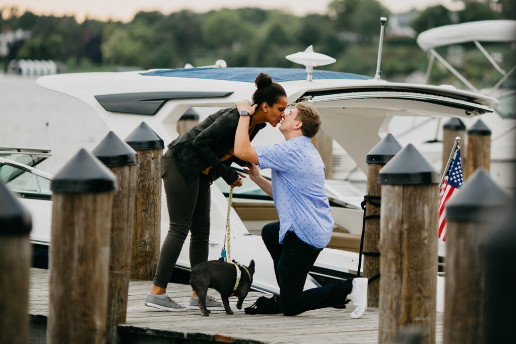 couple kissing on a boat dock during a surprise proposal with their French bulldog on a leash