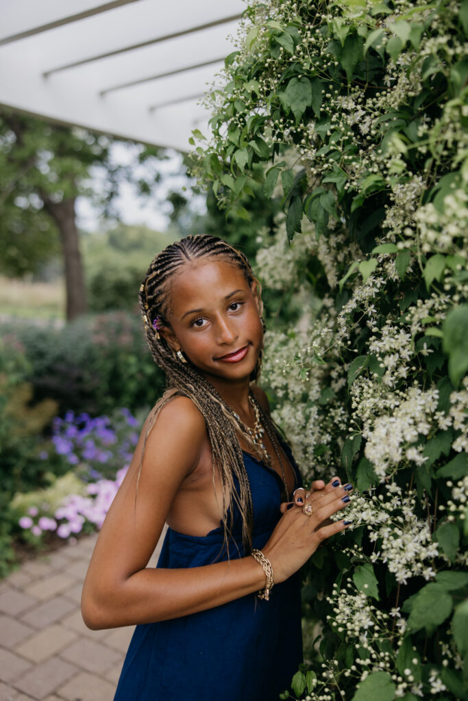 Senior standing beside a flowering vine-covered pergola, wearing a navy dress