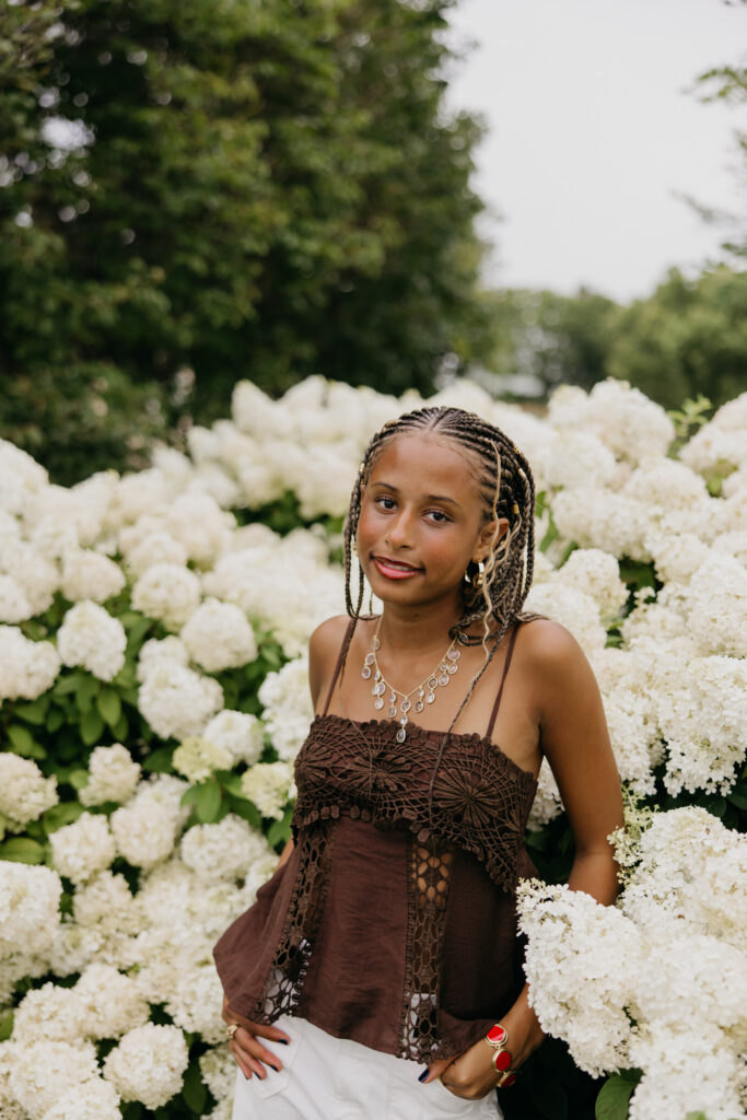 Senior standing in front of white hydrangea blooms, wearing a brown fringe top