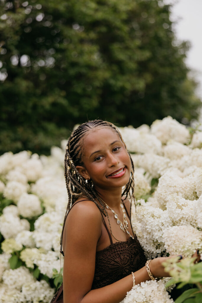 Senior standing in front of white hydrangeas, wearing a brown top