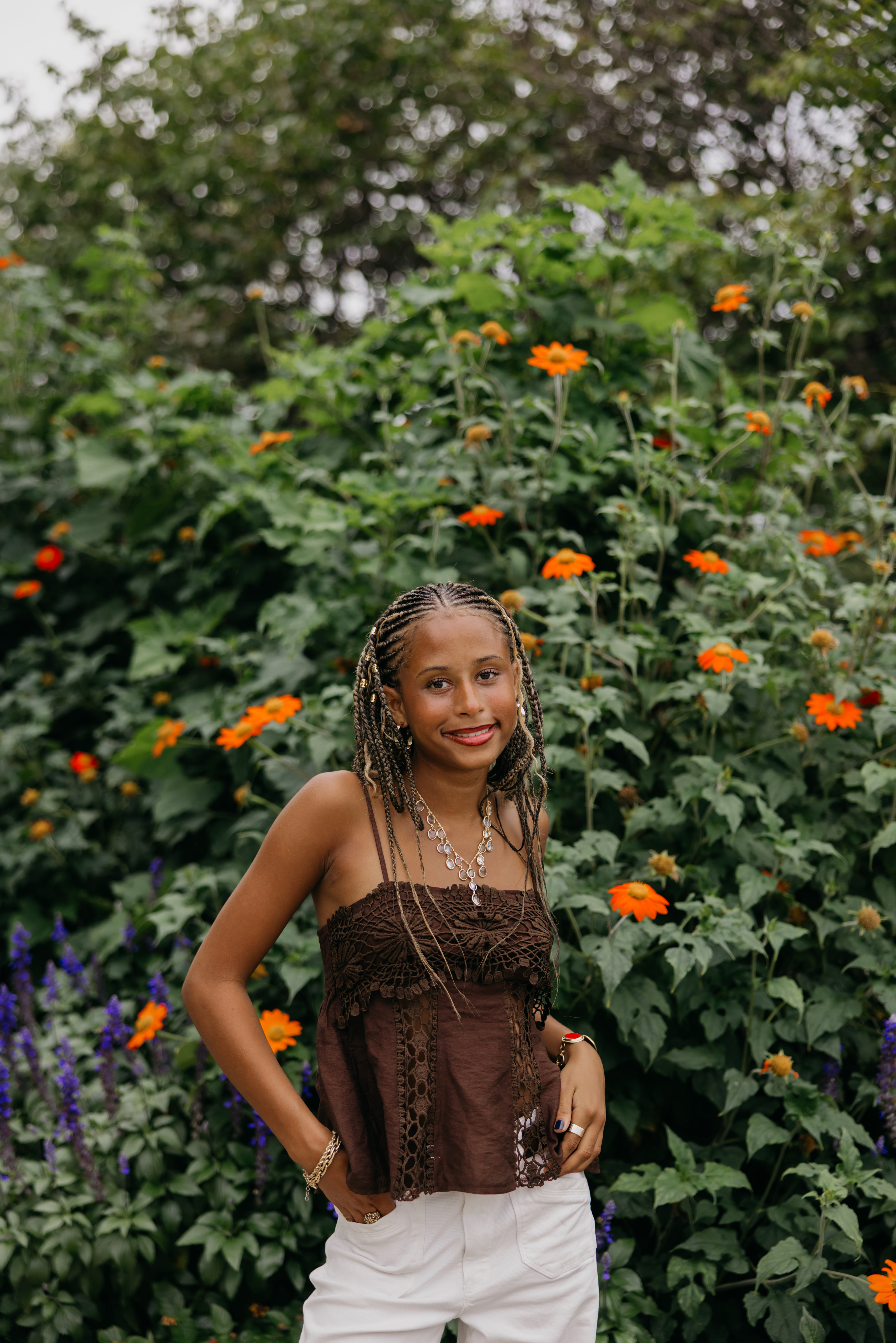 Senior standing in a garden bed of orange flowers, wearing a brown top