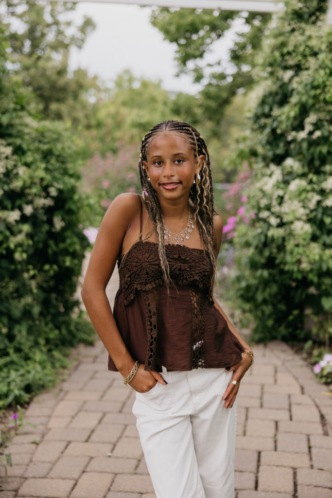 Senior standing on a brick garden path, wearing a brown top and white pants