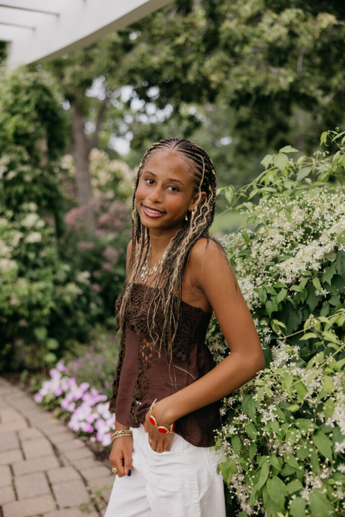 Senior standing beside white garden blooms, wearing a brown top