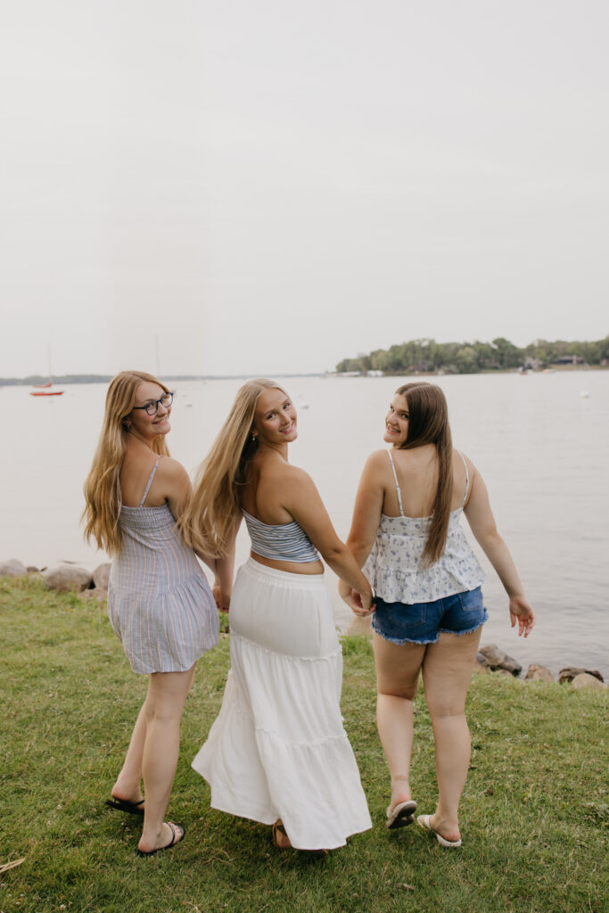 three senior friends walking hand in hand away from the camera toward the lake