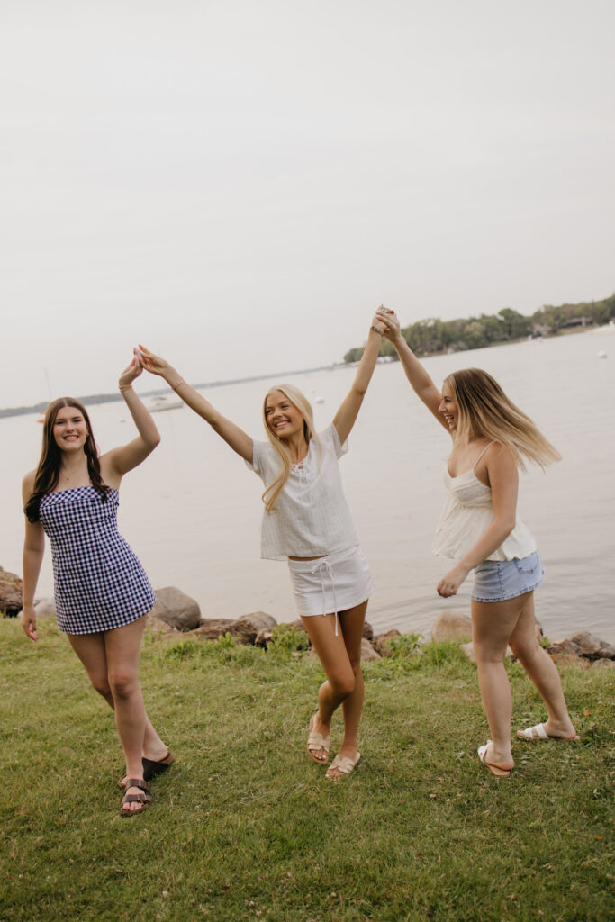 three friends dancing with joined raised hands on the grass by the lake