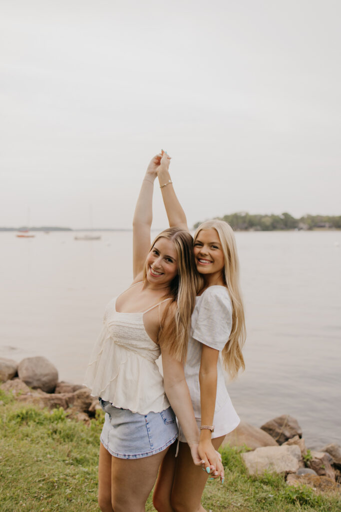 two senior friends laughing with one arm raised by the lake