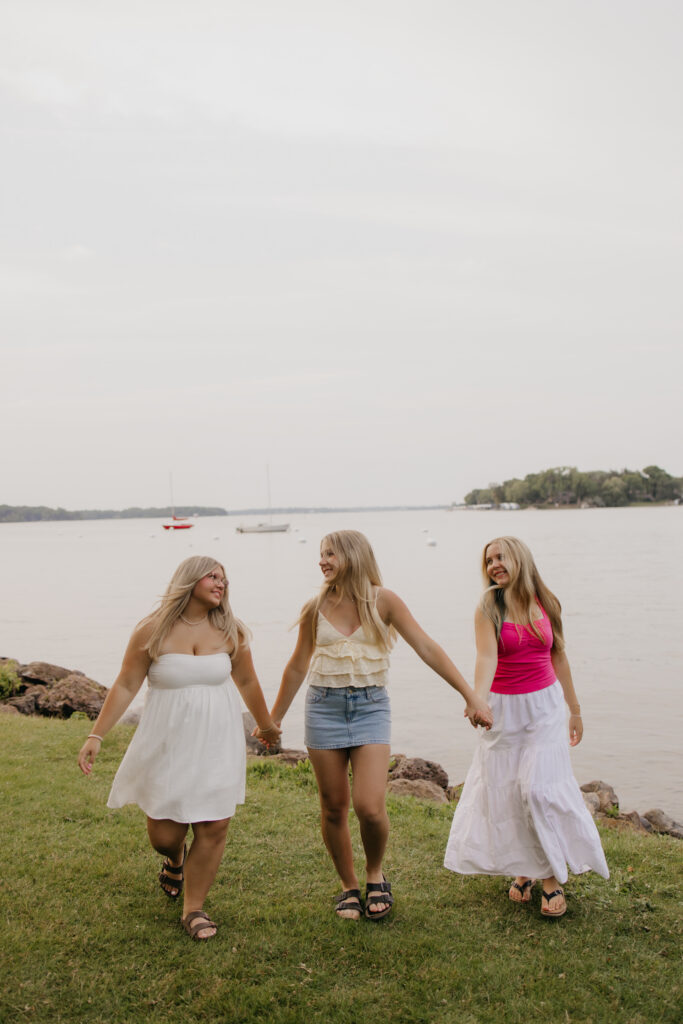 senior friend group photoshoot moment of three friends walking hand in hand by the lake
