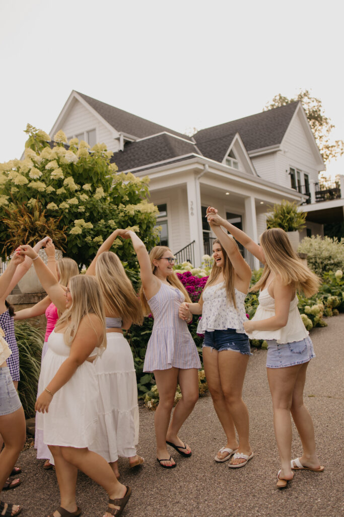 friend group forming a joined-hands arch a second time in front of hydrangeas