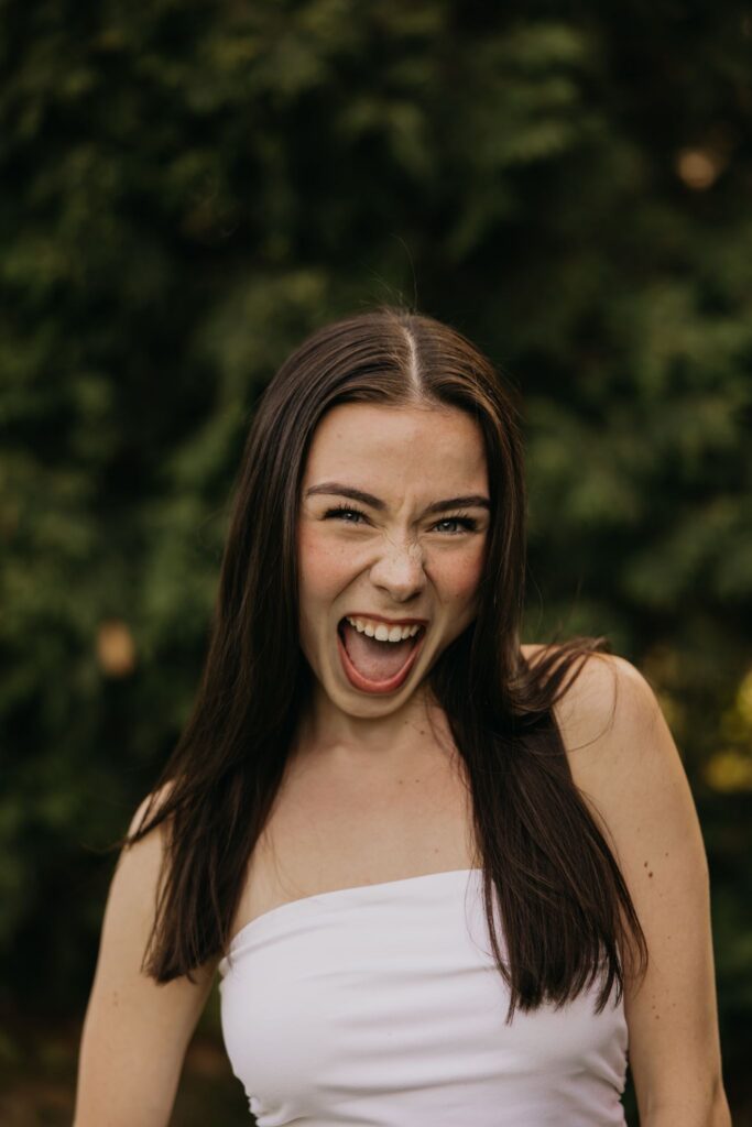 Senior girl in a white tube top laughing with tongue out for a candid senior portrait