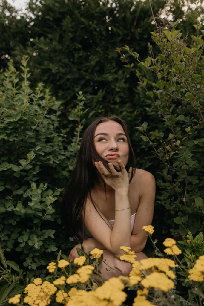 Senior girl kneeling among yellow flowers looking up in a bright, playful senior portrait