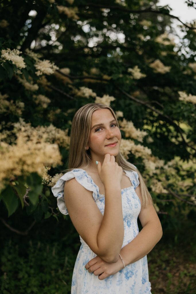 Senior girl in a blue floral dress resting her chin on her hand in a garden