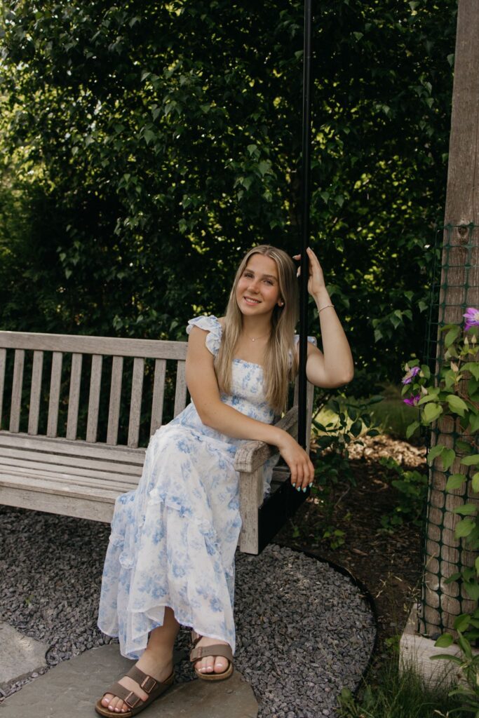 Senior girl in a blue floral dress sitting on a wooden garden bench