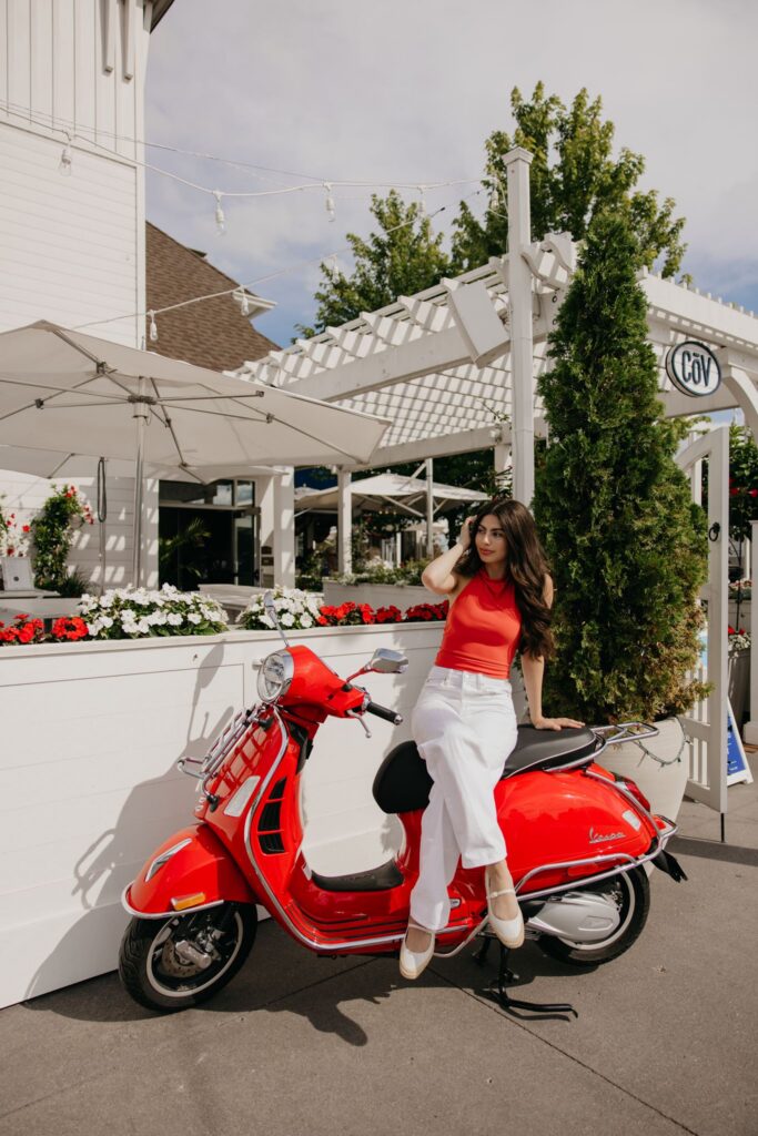 Senior girl sitting on a red Vespa scooter smiling for an urban senior photo session
