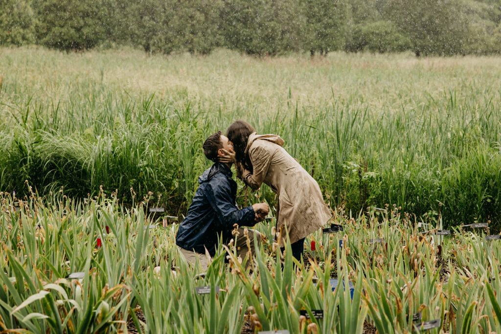 man kneeling to propose in the rain as his partner leans in to kiss him