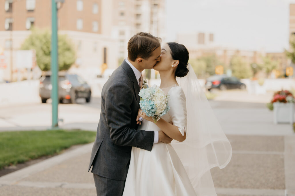 Bride and groom kiss outside on a sunny Minneapolis street corner near Central Lutheran Church