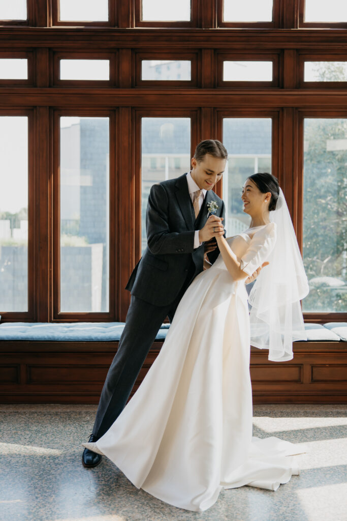 Groom dips bride again in front of the wood-framed windows, both smiling, at their American Swedish Institute wedding