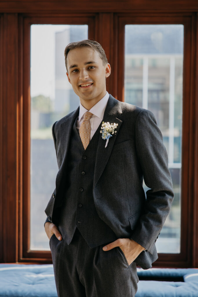 Groom smiles standing in front of a large wood-framed window with the Minneapolis skyline visible behind him