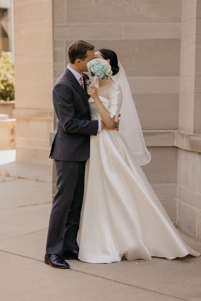 Bride and groom embrace and kiss against the stone facade of Central Lutheran Church in Minneapolis